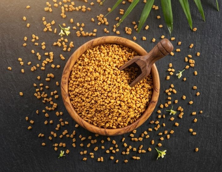 Fenugreek seeds in a wooden bowl with a scoop on dark slate